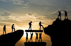people helping each other cross the bridge between two cliffs